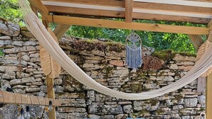 A covered outdoor seating area with a hammock, stone wall, and a blue cushioned sofa. - Country cottage with swimming pool in the Quercy Regional Park (Larnagol)