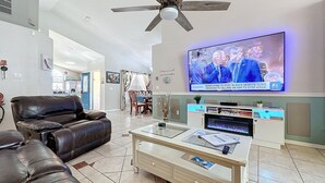 Een moderne woonkamer met een leren bank, een glazen salontafel en een aan de muur bevestigde televisie waarop een nieuwsuitzending wordt vertoond.