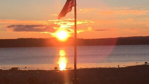 Flagstang med amerikansk flag mod en solnedgang over vand.
