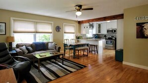 A spacious living area with a sofa, coffee table, and a dining table with chairs. A kitchen with modern appliances is visible in the background. - ☆Oakley's Oasis, a Dharma Dwellings Designed Home☆ (Rochester)
