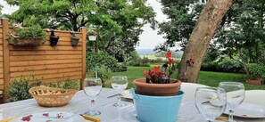 Un área de comedor al aire libre con una mesa preparada para dos personas, rodeada de follaje y una cerca de madera.