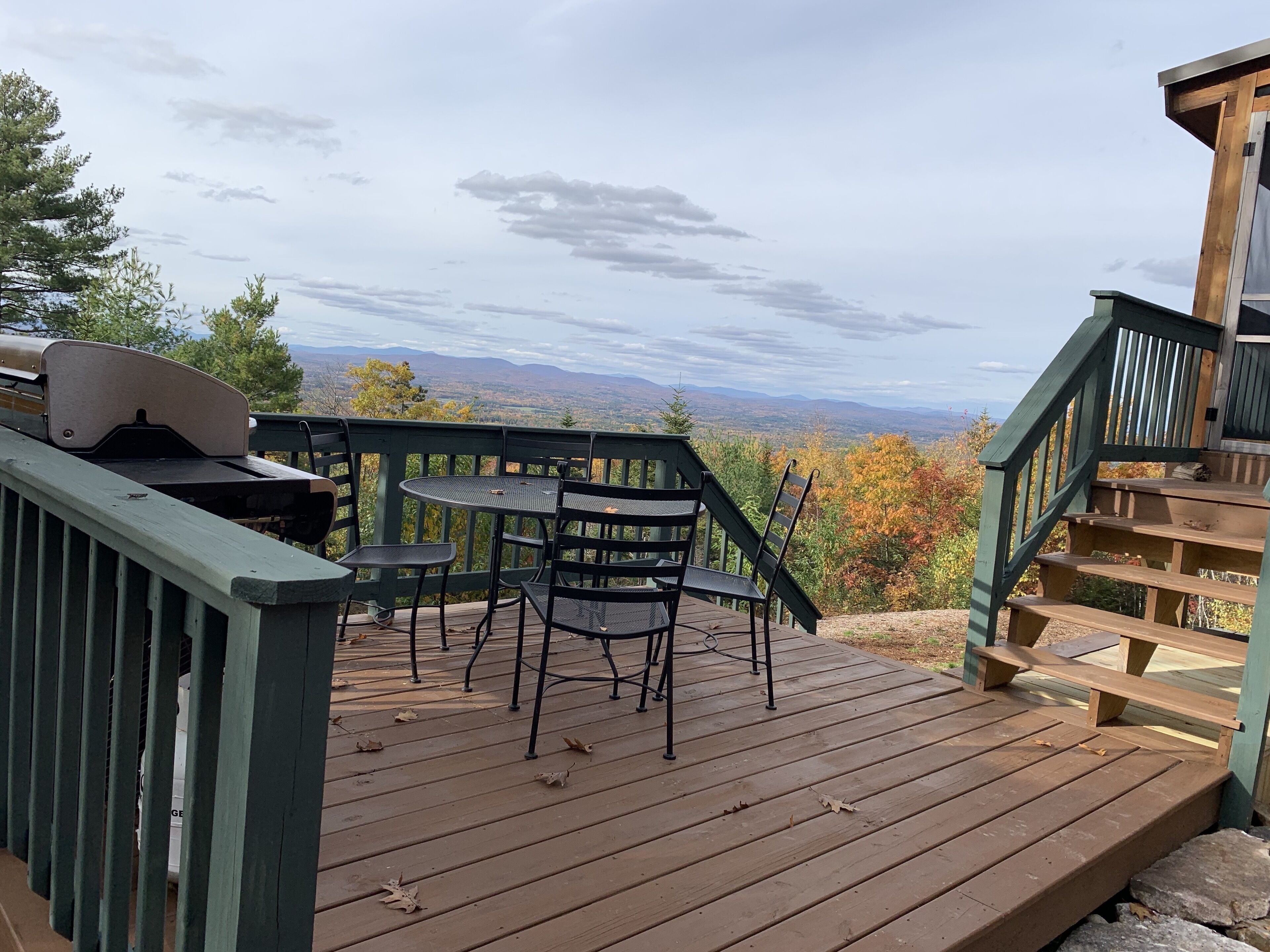 Terraza de madera con mesa y sillas, con vistas panorámicas a montañas y follaje otoñal.