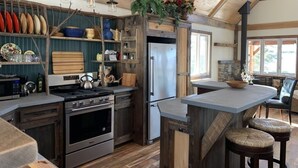A rustic kitchen with wooden beams, a large stove, a refrigerator, and a bar area with stools. - A soul soothing escape. Artistically built and lovingly maintained. (New Sharon)
