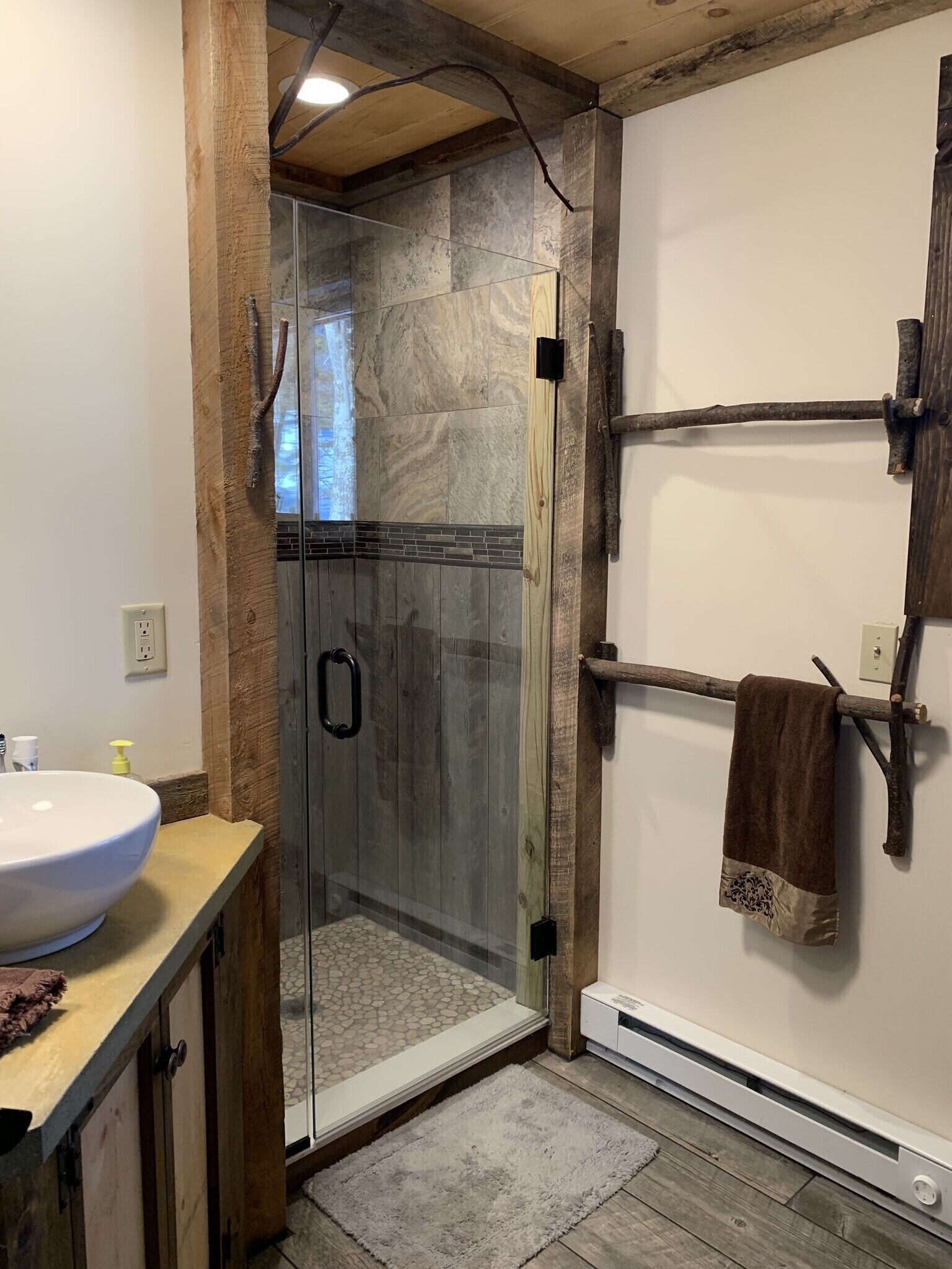 A bathroom with a glass-enclosed shower, wooden cabinets, a large white sink, and a towel rack.