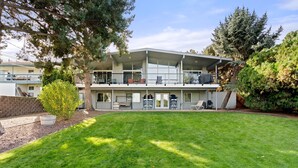 A two-story building with a flat roof and large windows. There is a well-maintained lawn in front, and a tree to the left. - Lg House w beautiful River View 2 stories, 5bd3bth (Kennewick)