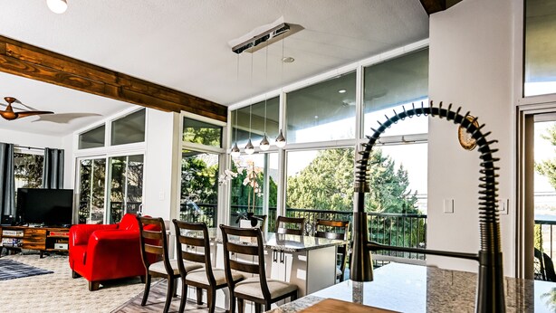 A modern living room with a red sofa, wooden chairs, a TV, and a kitchen area with a large window. - Lg House w beautiful River View 2 stories, 5bd3bth (Kennewick)