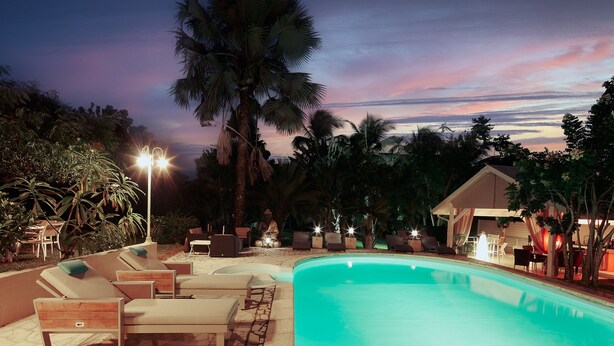 A swimming pool area with lounge chairs and a covered seating area, surrounded by palm trees and a sunset view. - Domaine de Néron - Daïquiri (Le Moule)