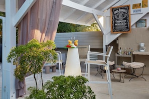 Una zona patio con tavolo e sedie, una piccola pianta e un cartello pubblicitario di whiskey Jack Daniel's.