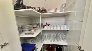 A compact kitchen with white cabinets, shelves stocked with plates, glasses, and kitchen utensils. - Beach house in São José da Coroa Grande, with Wi-Fi and TV. (São José da Coroa Grande)