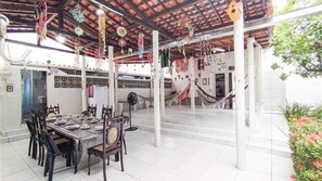 Uma ampla área de jantar com uma mesa comprida e cadeiras, teto com decorações penduradas e uma escada que leva a um andar superior.