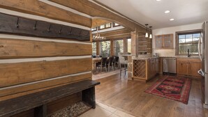 A rustic kitchen with wooden beams, a dining area with a bench, and a view of the outdoors. - Big Sky Vacation Rentals: PR Manitou 5 (Gallatin Gateway)