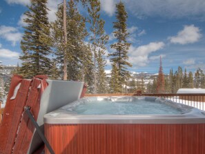A hot tub with a wooden exterior, surrounded by tall pine trees and a snowy mountain backdrop. - Big Sky Vacation Rentals: PR Manitou 5 (Gallatin Gateway)