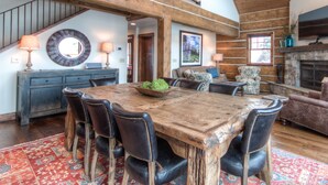 A spacious dining area with a large wooden table and leather chairs, a cozy living room with a fireplace, and a staircase leading to an upper level. - Big Sky Vacation Rentals: PR Manitou 5 (Gallatin Gateway)