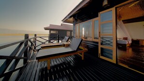 Eine Holzterrasse mit einer Liege und einem kleinen Tisch, mit Blick auf ruhiges Wasser.