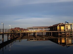 Une propriété située au bord de l’eau, dotée d’un quai s’étendant dans une zone d’eau calme, d’un espace extérieur couvert aménagé en salon et d’un bâtiment dont le toit est en pente.
