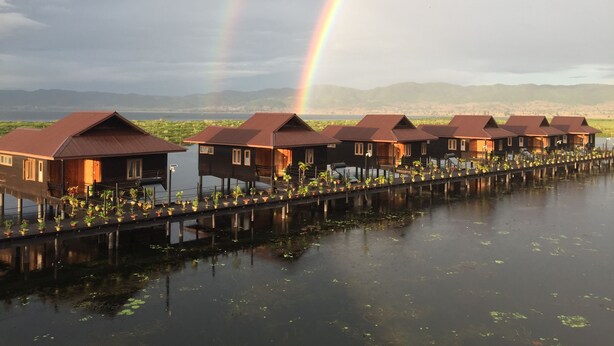 Eine Reihe von Bungalows über dem Wasser, im Hintergrund ein Regenbogen.