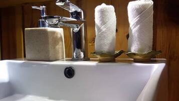 Un lavabo con grifo cromado, dos toallas blancas sobre un estante de madera y un jabonero.