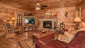 L’intérieur d’un chalet confortable, avec une cheminée, des murs en bois, un téléviseur et des sièges confortables.