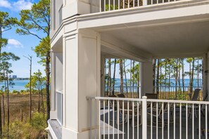 A white building with a balcony overlooking a body of water and trees.