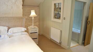 A bedroom with a bed, a nightstand with a lamp, a radiator, and a door leading to another room.