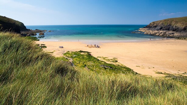 Une plage avec une eau d’un bleu limpide, un rivage sablonneux et des falaises verdoyantes.