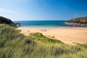 Ein Strand mit klarem, blauem Wasser, sandigem Ufer und grasbewachsenen Klippen.