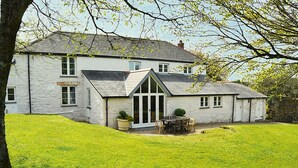 Une grande maison en pierre avec un toit en pente, une véranda et une pelouse bien entretenue.
