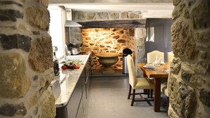 Une cuisine aux murs de pierre comprenant un coin repas, avec un évier en pierre, un grand récipient en pierre et une table à manger avec des chaises.