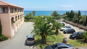 A parking area with several cars, palm trees, and a building with arched windows. - Marina di Bravone beach, Linguizzetta, Corsica, France (Linguizzetta)