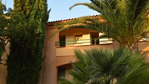 A building with a balcony, a palm tree, and a tall evergreen tree. - Marina di Bravone beach, Linguizzetta, Corsica, France (Linguizzetta)