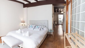 Een slaapkamer met een groot bed, nachtkastjes, een houten bankje en uitzicht op een balkon.