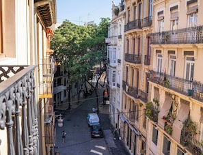 A narrow street with buildings on either side, a parked car, and a person walking.