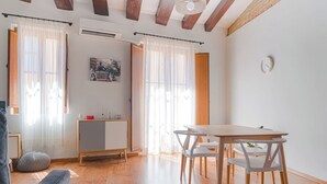 A modern living room with a dining area, wooden flooring, and a large window with sheer curtains.
