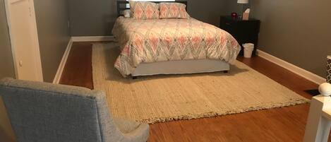 A bedroom with a bed, a chair, a nightstand, and a window.