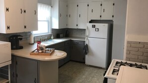 Una cocina compacta con armarios blancos, un refrigerador, una estufa y una cafetera.