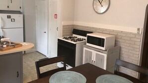Cocina compacta con estufa a gas, microondas y un reloj en la pared.