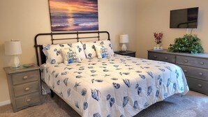 A bedroom with a bed, nightstands, a dresser, a TV, and a painting of a sunset over the ocean.