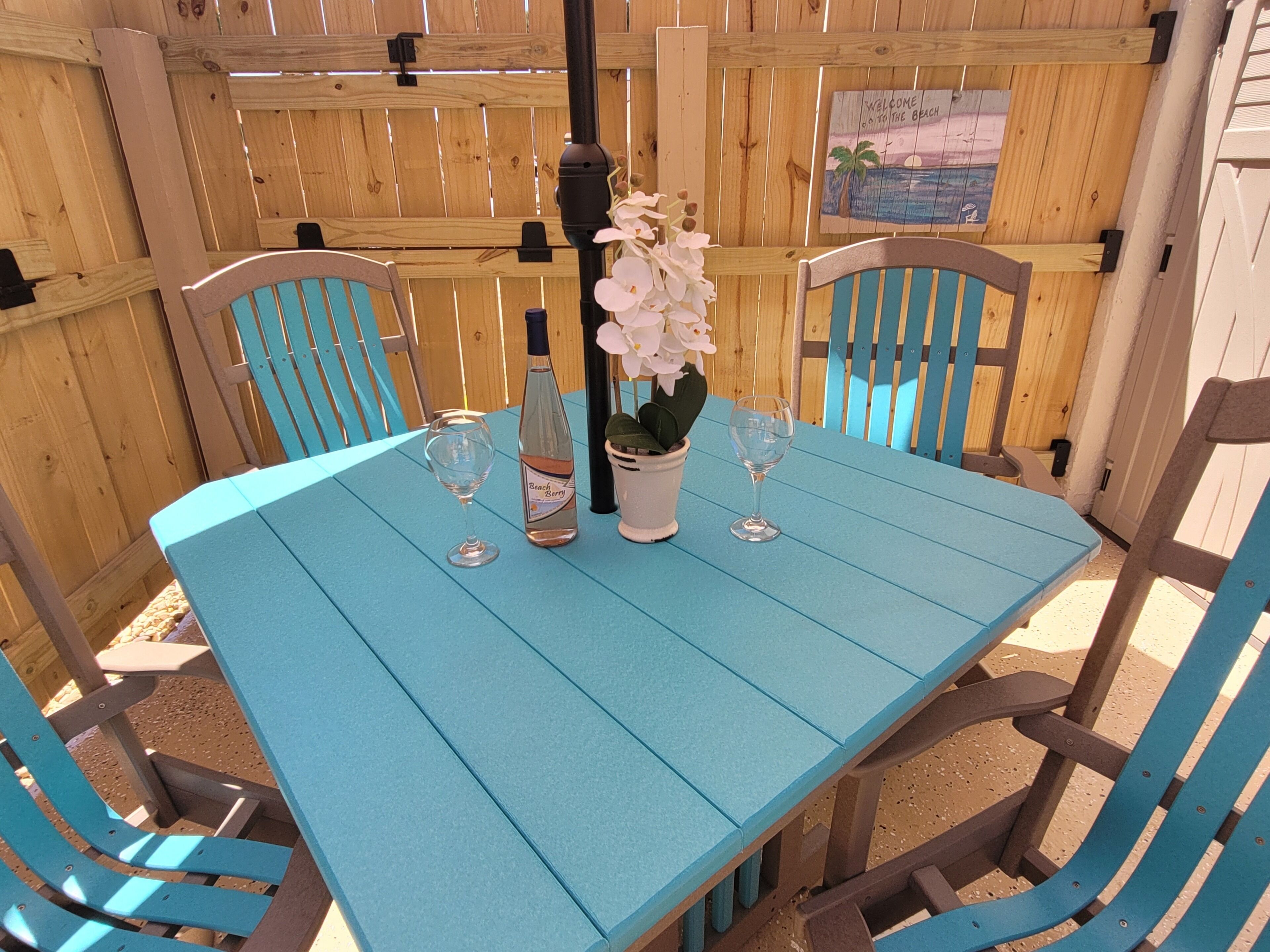 Ein blauer Tisch im Freien mit zwei Weingläsern, einer Flasche Beach Berry Wein und einer Topforchidee.