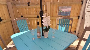 A blue outdoor table with two wine glasses, a bottle of Beach Berry wine, and a potted orchid.