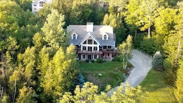 Suuri, kaksikerroksinen talo, jonka ympärillä on tiheä metsä. Talolle johtaa selkeästi näkyvä ajotie, ja etupihalla on pieni lampi.