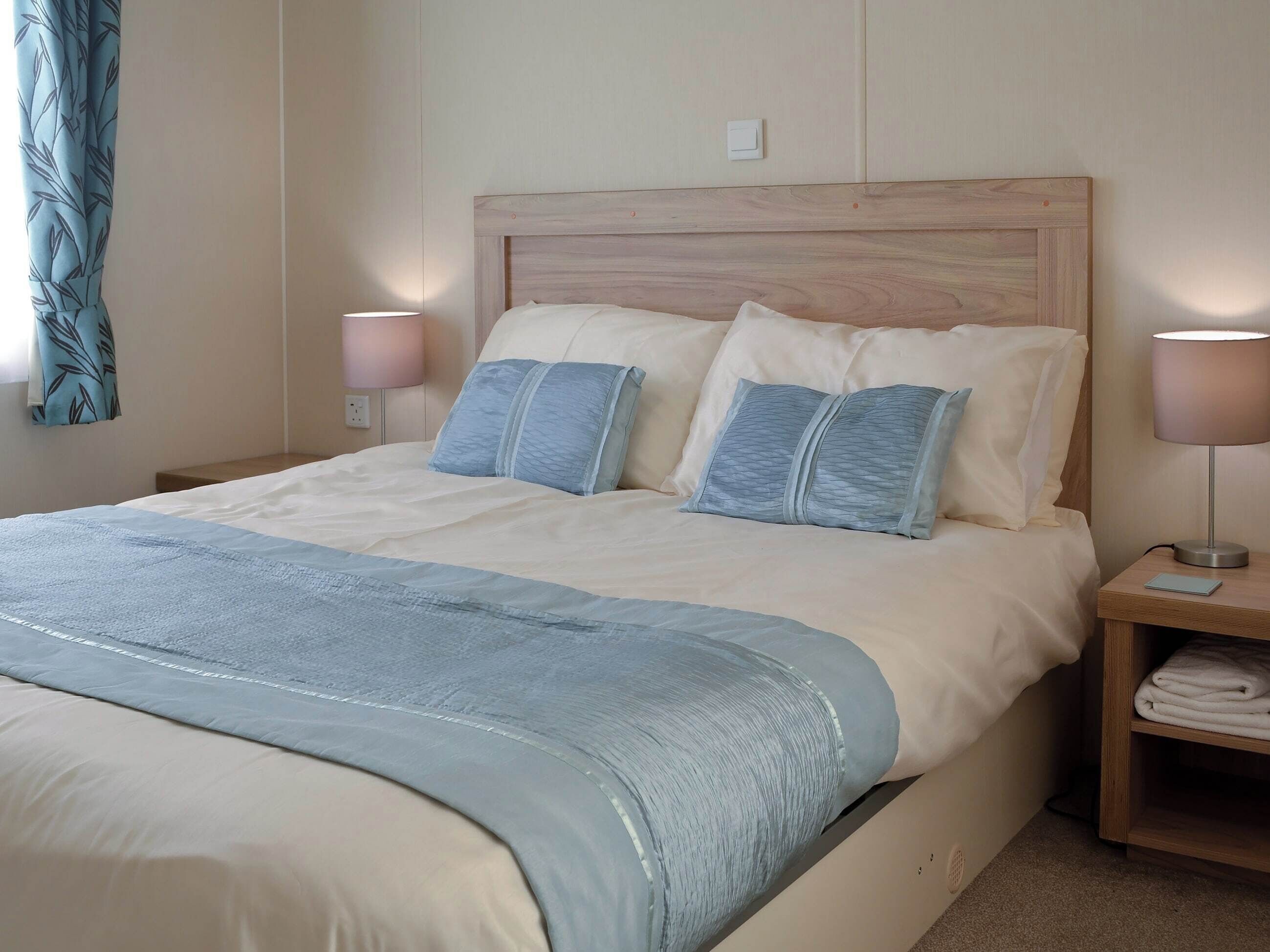 A neatly made bed with a blue and white bedspread, two bedside lamps, and a wooden nightstand with a folded towel.
