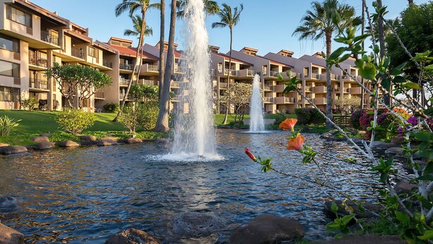 Ein Hotel mit mehreren Balkonen, einem Wasserspiel mit Springbrunnen und üppiger Bepflanzung.