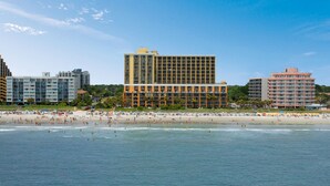 A beachfront hotel with multiple floors, a sandy beach in the foreground, and a clear blue sky. - Beautiful Caravelle Resort Oceanfront Double Efficiency (Myrtle Beach)