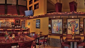 A bar area with a counter, chairs, and tables. There are framed artworks on the walls. - Beautiful Caravelle Resort Oceanfront Double Efficiency (Myrtle Beach)