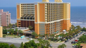 A multi-story hotel with a prominent glass facade, located near a beach with visible ocean views. - Beautiful Caravelle Resort Oceanfront Double Efficiency (Myrtle Beach)