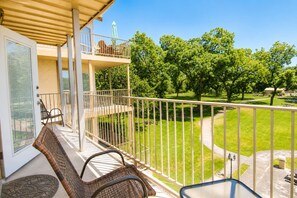 A balcony with wicker furniture, a view of a park with trees and a pathway, and a clear sky.