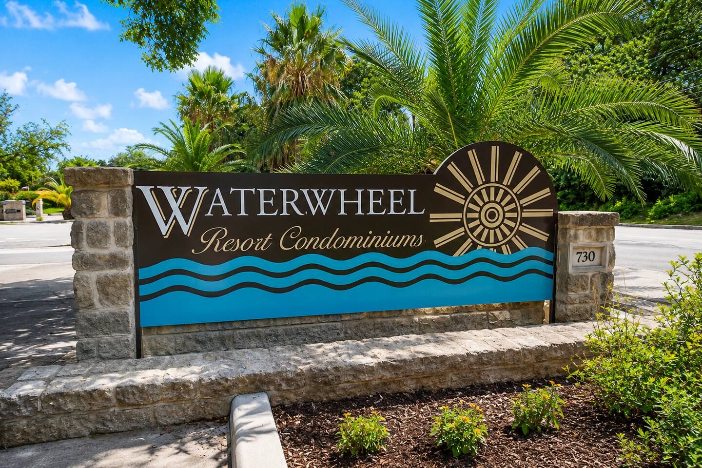 A sign for Waterwheel Resort Condominiums with a sun and waves design.