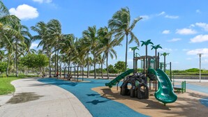 Un parque infantil con tobogán y estructuras de escalada, rodeado de palmeras y un cielo despejado.