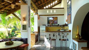 A kitchen with a tiled floor, a refrigerator, and a sink. There is a dining area with a round table and chairs. - Romantic Zone, best location; with daily maid and cook service included! (Puerto Vallarta)