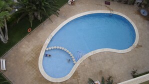 An aerial view of a swimming pool with a curved edge, surrounded by a tiled deck and palm trees. - BALI-BENIDORM HOTEL FRONT APARTMENT (Finestrat)